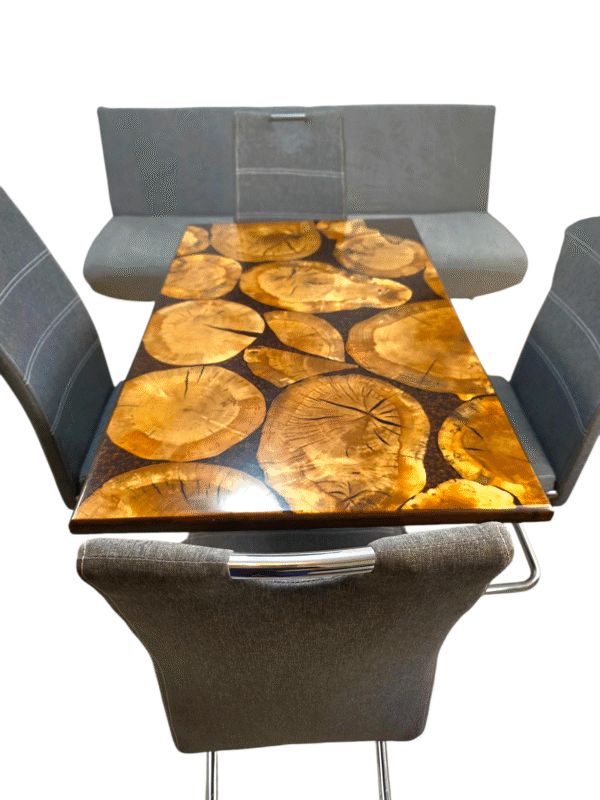 A unique and handcrafted epoxy resin table. The tabletop features a mosaic of irregularly shaped, light brown wood slices embedded within a dark brown, glossy epoxy resin. Some of the wood slices display visible tree rings and natural cracks. The resin is smooth and reflective, catching the light. The table has a dark brown wooden edge and rests on sturdy black legs. The table is a stylish, nature-inspired piece of furniture with a modern touch.