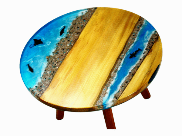 A small resin epoxy coffee table featuring a tabletop with Maple wood edges and a vibrant blue epoxy resin river in the center. Embedded within the translucent blue resin are orange starfish and dolphins, enhancing the table's beach-themed aesthetic.